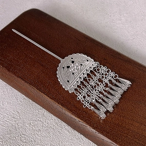 Ethnic style silver hair stick with hollow carving and metallic tassels on wood