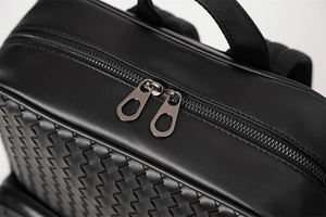 Detailed macro view of black woven leather backpack featuring smooth double metal zippers