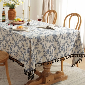 Close-up of blue floral tablecloth with black fringe on a rustic wooden dining table