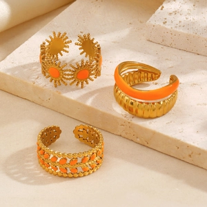 Three gold stainless steel rings with orange enamel in sun and leaf designs on stone