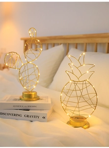 Golden iron pineapple and cactus LED decorative lamps on white bedding in cozy bedroom