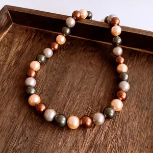 Retro mehrfarbige Perlenkette mit Metallglanz auf Vintage-Tablett aus dunklem Holz
