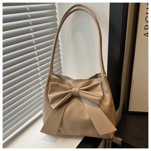 Close-up of a beige leather shoulder bag featuring a large decorative bow and matte finish