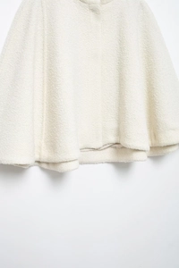 Detailed close-up showing the creamy white boucle tweed texture of the jacket hem