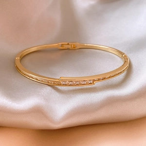Detail eines vergoldeten Armreifs mit Zirkonia-Steinen auf Seidenhintergrund