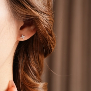 Close-up of elegant cross-shaped zircon stud earrings worn on a model's earlobe
