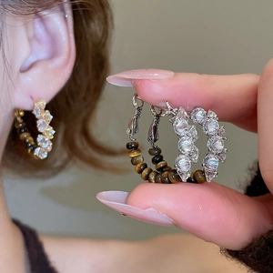 Twisted silver hoop earrings featuring alternating clear crystals and brown tiger eye beads