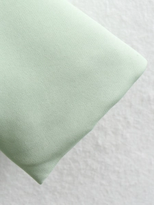 Detailed macro shot showing the fine canvas texture of the light green blazer fabric