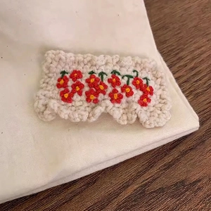 Detail of handmade crocheted rectangular clip with red floral embroidery on cream wool