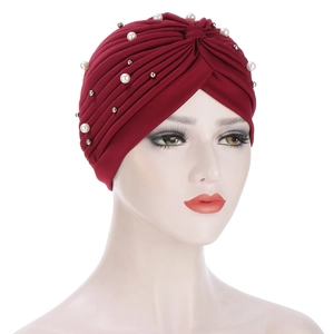Close-up of pleated burgundy turban hat with white faux pearls on display mannequin