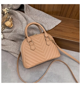 Detailed close-up of V-quilted texture and gold zipper on elegant beige shell bag