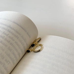 Close-up of gold S925 silver hoop earrings with black teardrop gemstone on book pages