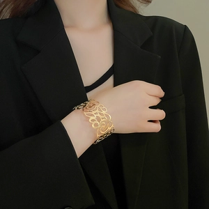 Detailed view of wide gold hollow rose patterned cuff bracelet on a model wrist