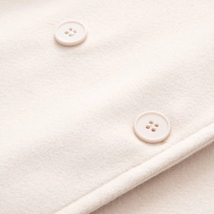 Vue macro du tissu en laine crème avec deux boutons ronds assortis à quatre trous