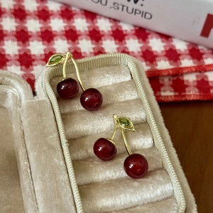 Macro shot of dark red cherry earrings with gold leaves on beige velvet cushion