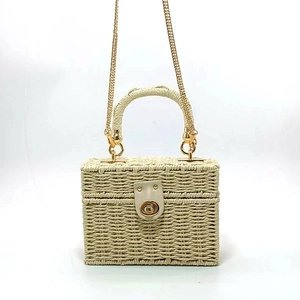 Detail of beige woven straw box bag featuring a gold twist-lock and metal chain strap