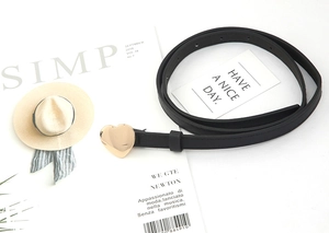 Detail of a thin black leather belt with a polished gold heart-shaped buckle on a magazine