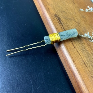 Macro shot of green crystal slice hair pin with gold wire wrapping on wood surface