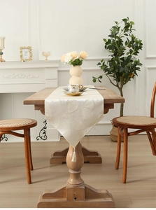 Detail of elegant leaf jacquard table runner with decorative tassel on a wooden table