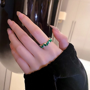 Détail d'une bague plaquée or avec zircon carré vert et diamants sur la main d'une femme