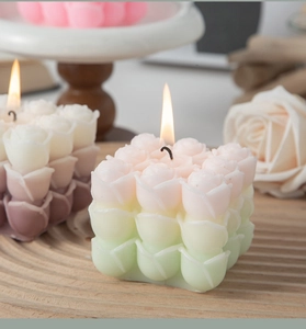 Close-up of burning pink and green gradient rose cube candle with wooden tray decor