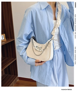 Detail of cream pleated shoulder bag with pearl chain and bow charm on a model