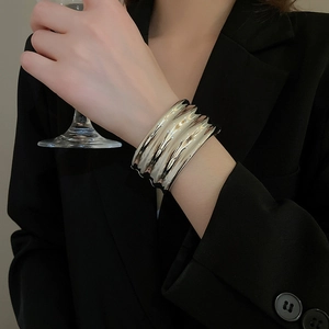 Detail of a wide silver wavy metal bracelet worn on a wrist with a modern irregular texture