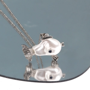 Macro detail of fish pendant with baroque pearl body and blue gemstone eye on mirror surface