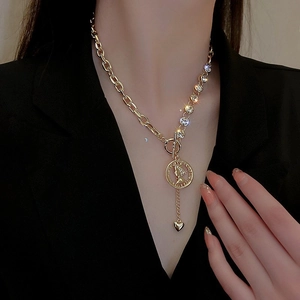 Dettaglio di collana vintage dorata con chiusura a barra, moneta e ciondolo a cuore