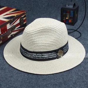 Detailed texture of beige woven sun hat featuring a black ribbon with decorative lettering