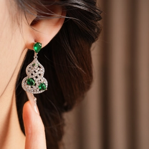 Macro shot of silver gourd earrings with green gemstones and white pearls on a model ear
