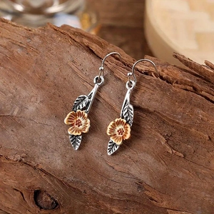Close-up of two-tone leaf and flower earrings with vintage texture on wood