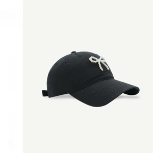 Detail showing a black cotton baseball cap featuring a white pearl bow embellishment