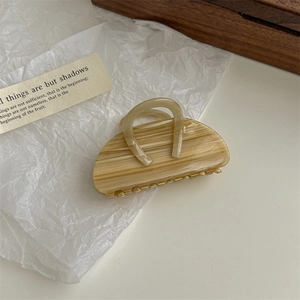 Detail of beige marble-patterned hair claw clip with double ring design on a prop card