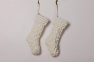 Detailed view of two white cable knit Christmas stockings with ribbed cuffs hanging decor