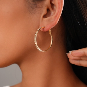 Close-up of a model wearing a large gold hoop earring with pavé-set shimmering crystals