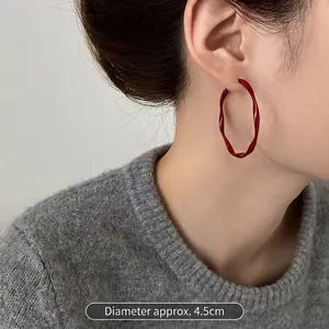 Detail view of 4.5cm red wavy twisted hoop earring on model with grey knitwear