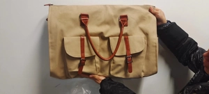 Vue détaillée du sac de voyage en toile beige avec anses en cuir brun et deux poches avant