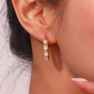Close-up of gold U-shaped hoop earrings with graduated pearls on a female model