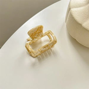 Detail of a square tortoiseshell hair claw clip with beige marble pattern and gold text