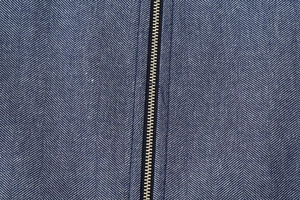 Detail von dunkelblauem Fischgrätstoff und goldenem Metallreißverschluss an der Jacke