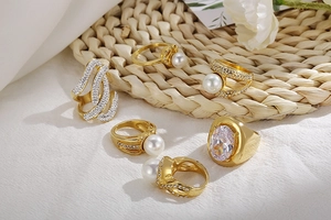 Detailed view of gold pearl and rhinestone stacking rings on a woven straw background