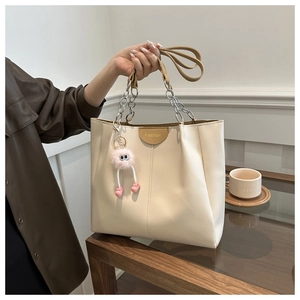 Dettaglio borsa shopper crema con catena argento e ciondolo di peluche rosa su legno