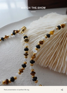 Detail of beaded necklace with tiger eye stone and gold lobster clasp on shell
