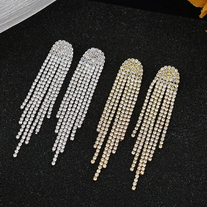 Detail of long tassel rhinestone earrings in gold and silver finish on black background