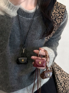 Three leather mini pouches in black, burgundy and brown on a grey knitted sweater background