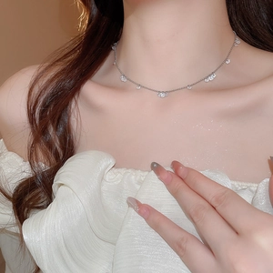 Close-up of a silver stainless steel necklace with small zircon flowers worn by a model