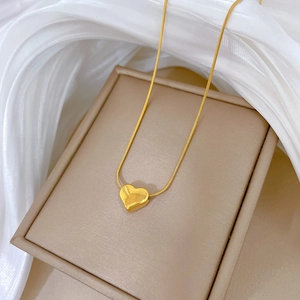 Detail of golden heart pendant on snake chain necklace resting on jewelry box