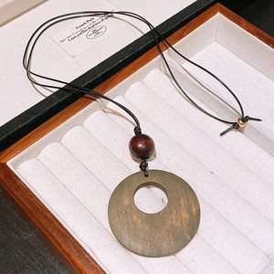 Detail of round wooden pendant with black cord in a beige lined jewelry gift box