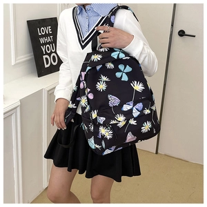 Detail of black backpack with daisy and butterfly prints worn by a model in casual setting
